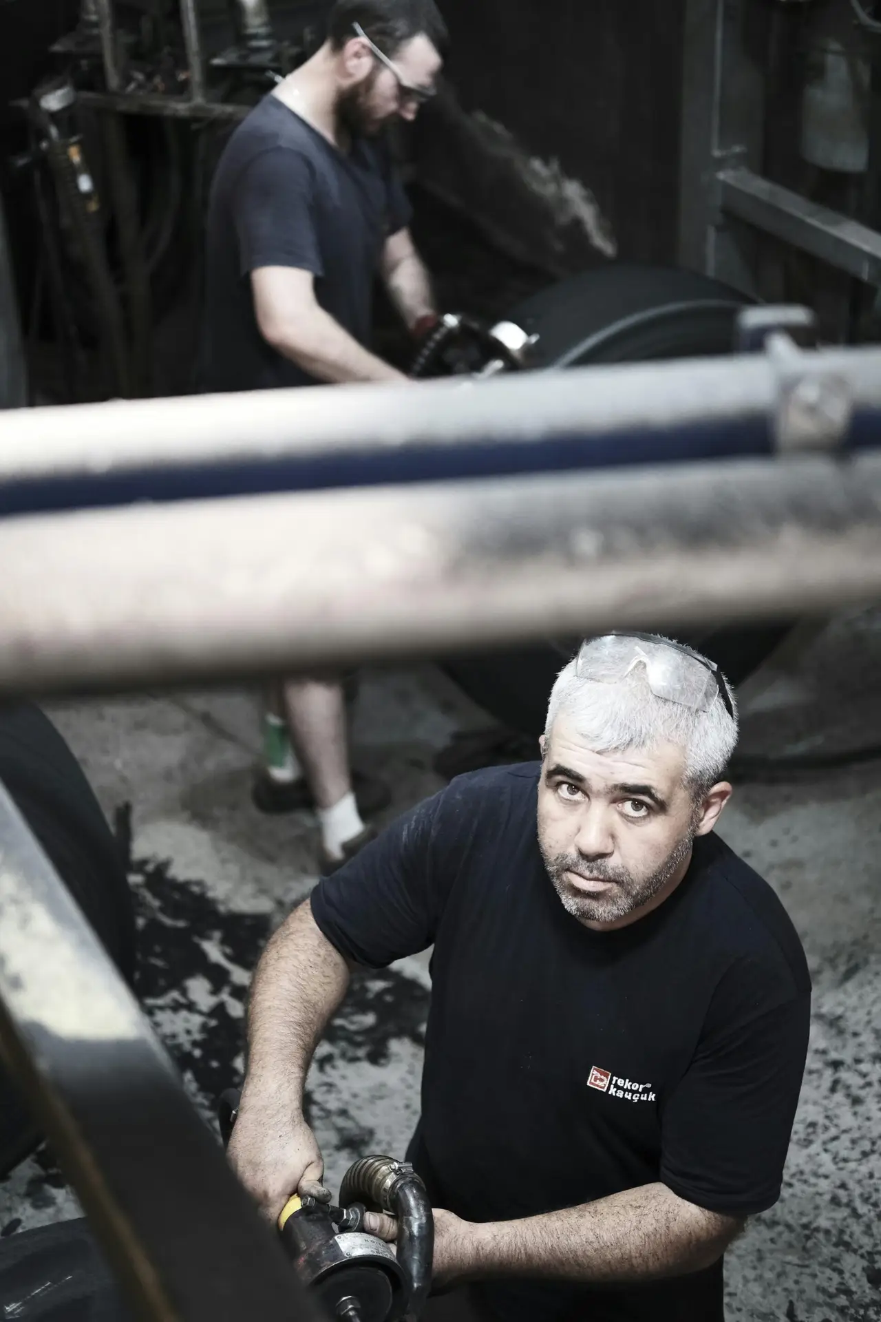Two industrial workers handling large machinery in a dimly lit factory setting.