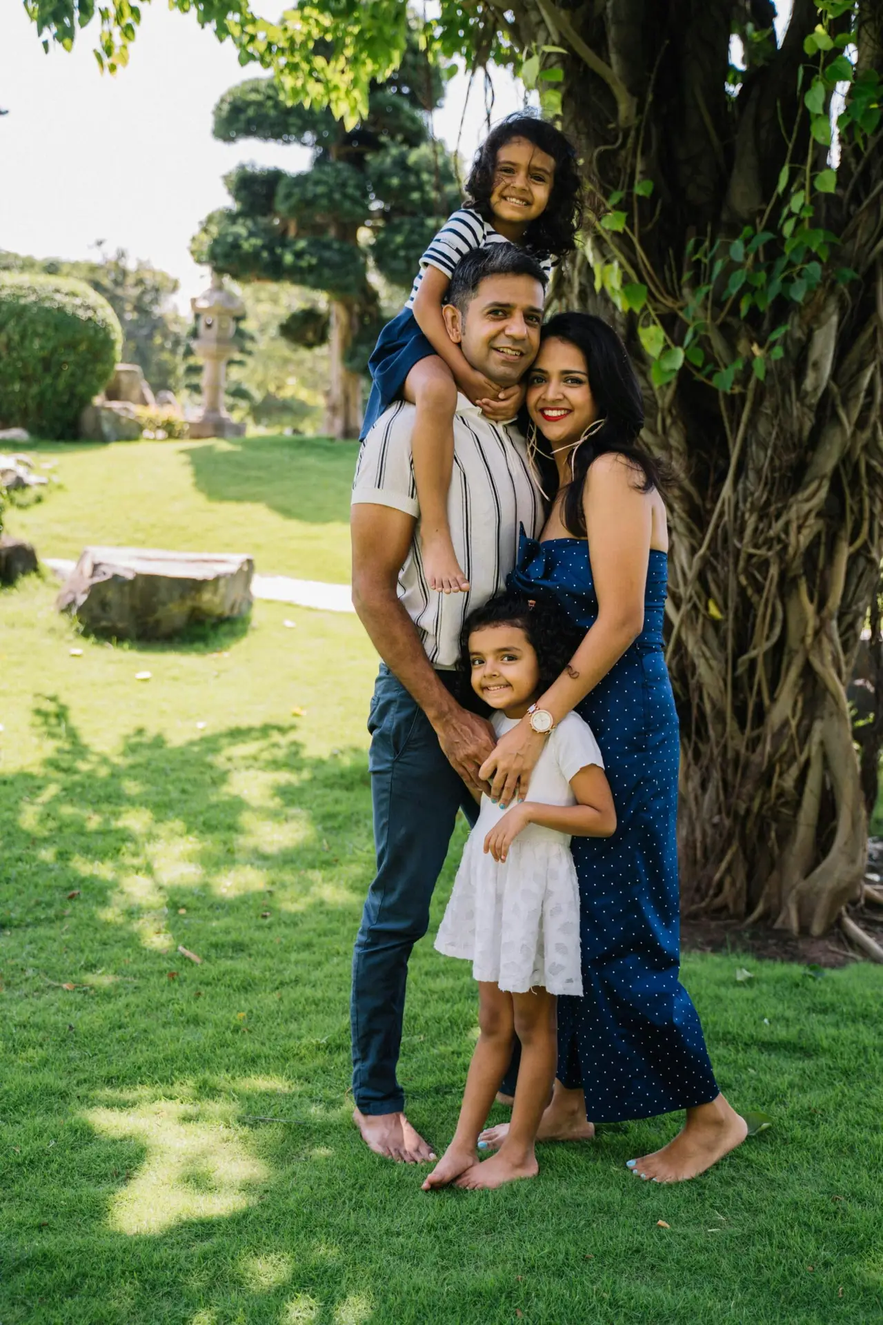 Smiling family of four enjoying a sunny day under a tree in the park.